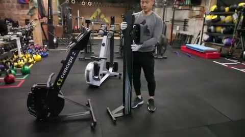 man standing a rowing machine upright to store it in a gym, face visible