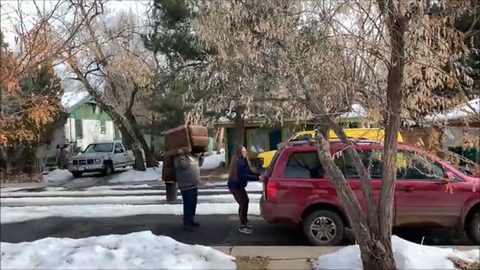 person carrying a brown recliner on their back to an SUV on a snowy street
