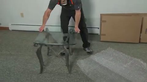 mover carefully lifting a glass tabletop off its wrought-iron base