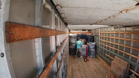 mover using a hand truck to load furniture deep inside a long moving truck