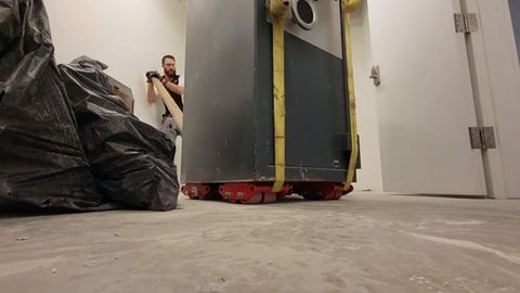 heavy safe strapped on machine skates guided down a hallway, face visible
