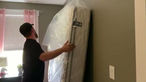 mover sliding a plastic mattress bag onto a mattress, face visible