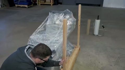 worker building a wooden crate around a shrink-wrapped item, face visible