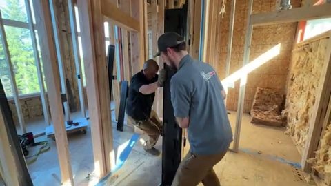 two movers carrying a tall black safe through a framed doorway, face visible