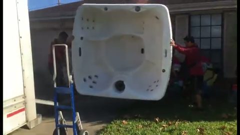 two movers standing a hot tub upright beside the moving truck