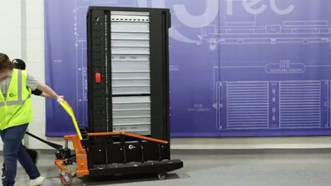 worker rolling a server rack on a pallet jack across a facility